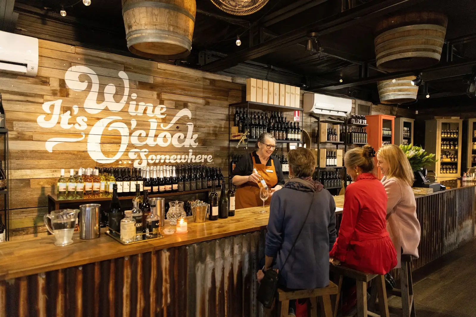 A staff member pours a drink for three guests seated at a timber bar