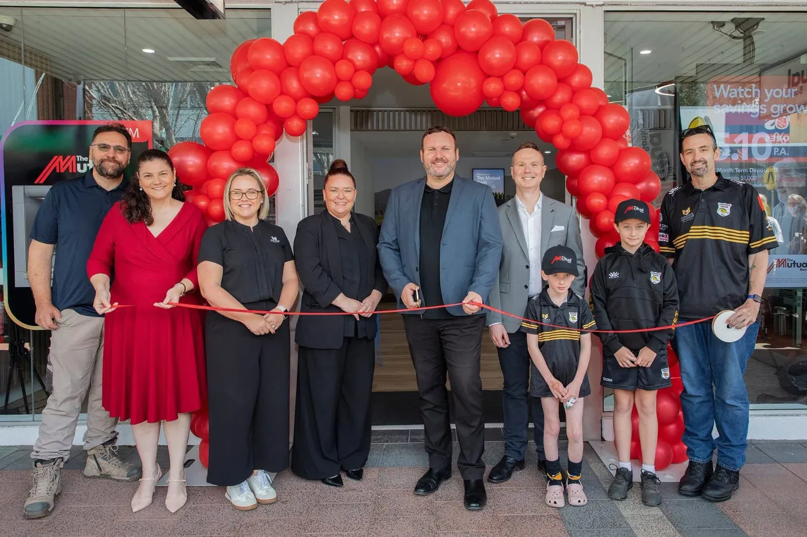 The Mutual Bank team and guests cutting the ribbon under a red balloon arch at the branch opening