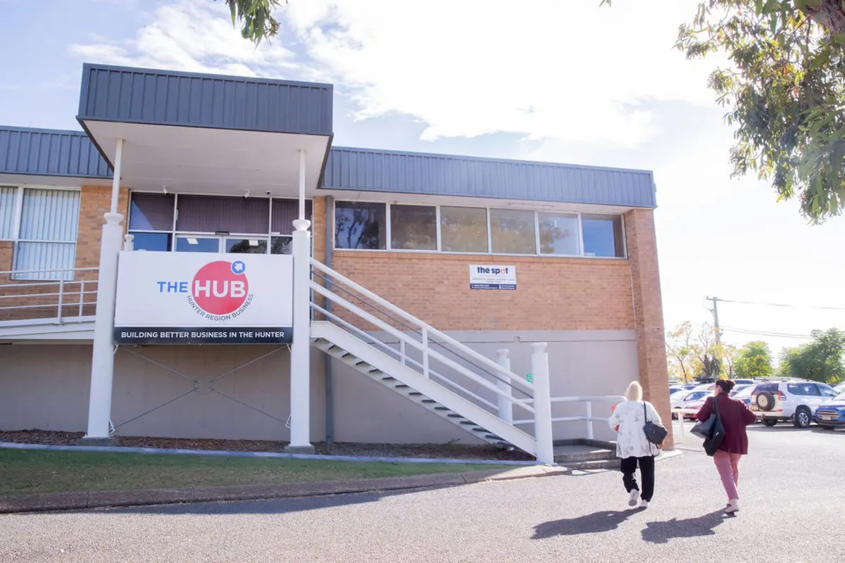 Two people walking in to the Hub building in Kurri Kurri, past the stairs and signage